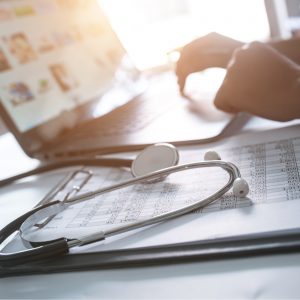 Hands working on laptop with stethoscope and chart in foreground