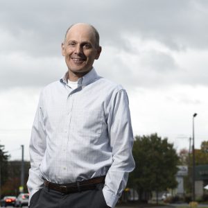 Man with hands in pockets standing outside smiling at camera