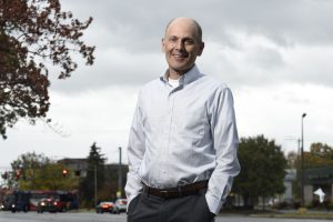 Man with hands in pockets standing outside smiling at camera